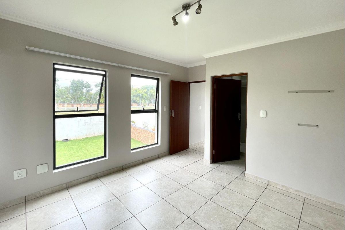 A bright, empty bedroom featuring neutral tiled flooring, large aluminium-framed windows, and clean finishes, ready for personalization.