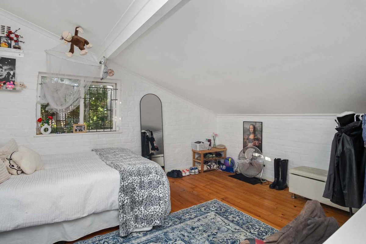 A bedroom featuring a sloped ceiling, exposed white-painted brick walls, and original timber flooring, providing a cozy and character-filled living space.
