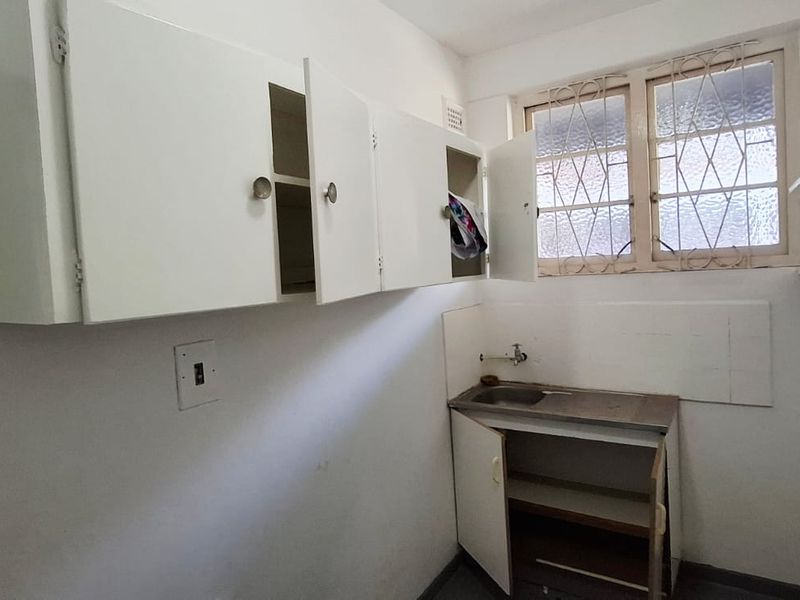 A functional scullery or utility area featuring built-in cabinetry, a stainless steel sink, and fixed shelving, requiring cosmetic updates to improve its condition.
