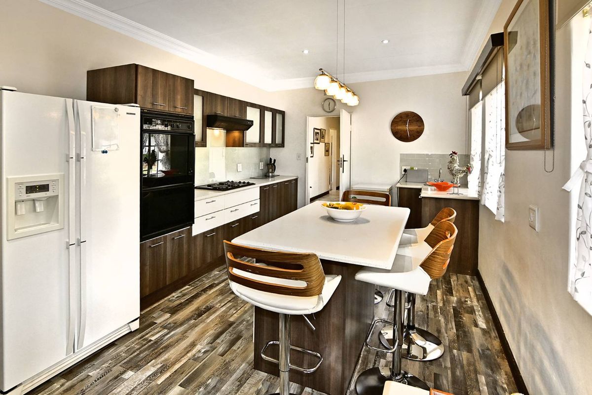 Modern kitchen featuring dark wood cabinetry, a central island with seating, built-in oven, gas hob, and durable laminate flooring.