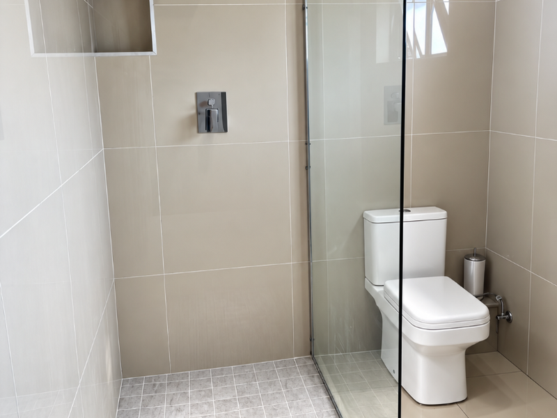 Modern bathroom featuring a walk-in shower with a glass screen, rain shower head, built-in niche, and neutral wall and floor tiling.