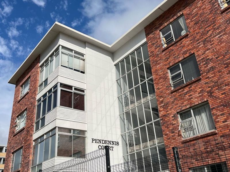 Exterior view of Pendennis Court apartment building featuring a brick facade, large glass window sections, and secure perimeter fencing.