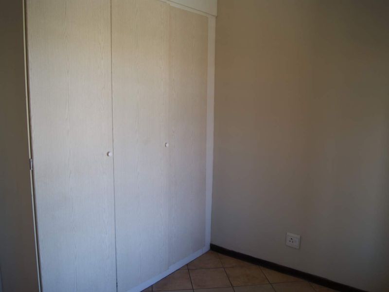 A clean, empty bedroom featuring neutral walls, tiled flooring, and built-in cupboards, offering a blank canvas for personalization.