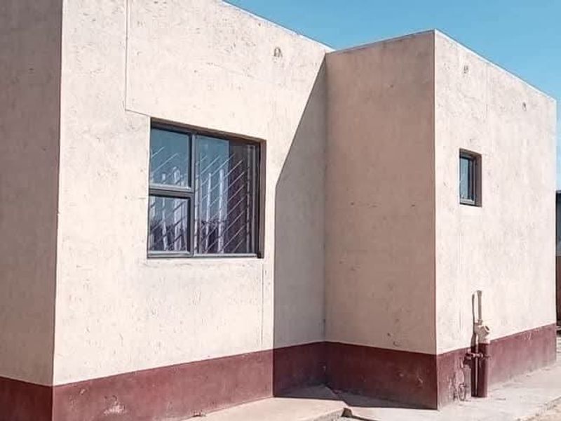 Rear exterior view of the house featuring plastered walls, aluminium window frames with security bars, and exposed external plumbing.