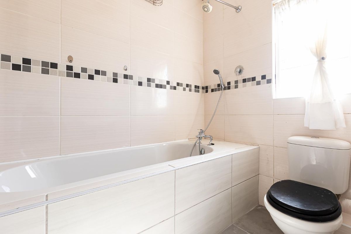 A functional bathroom featuring a built-in bathtub with shower attachment, a toilet, and neutral wall tiling with a decorative mosaic accent border.