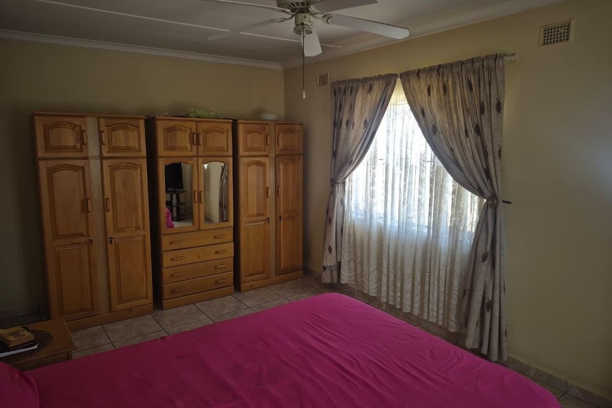 A bedroom featuring tiled flooring, a ceiling fan, and built-in wooden cupboards.