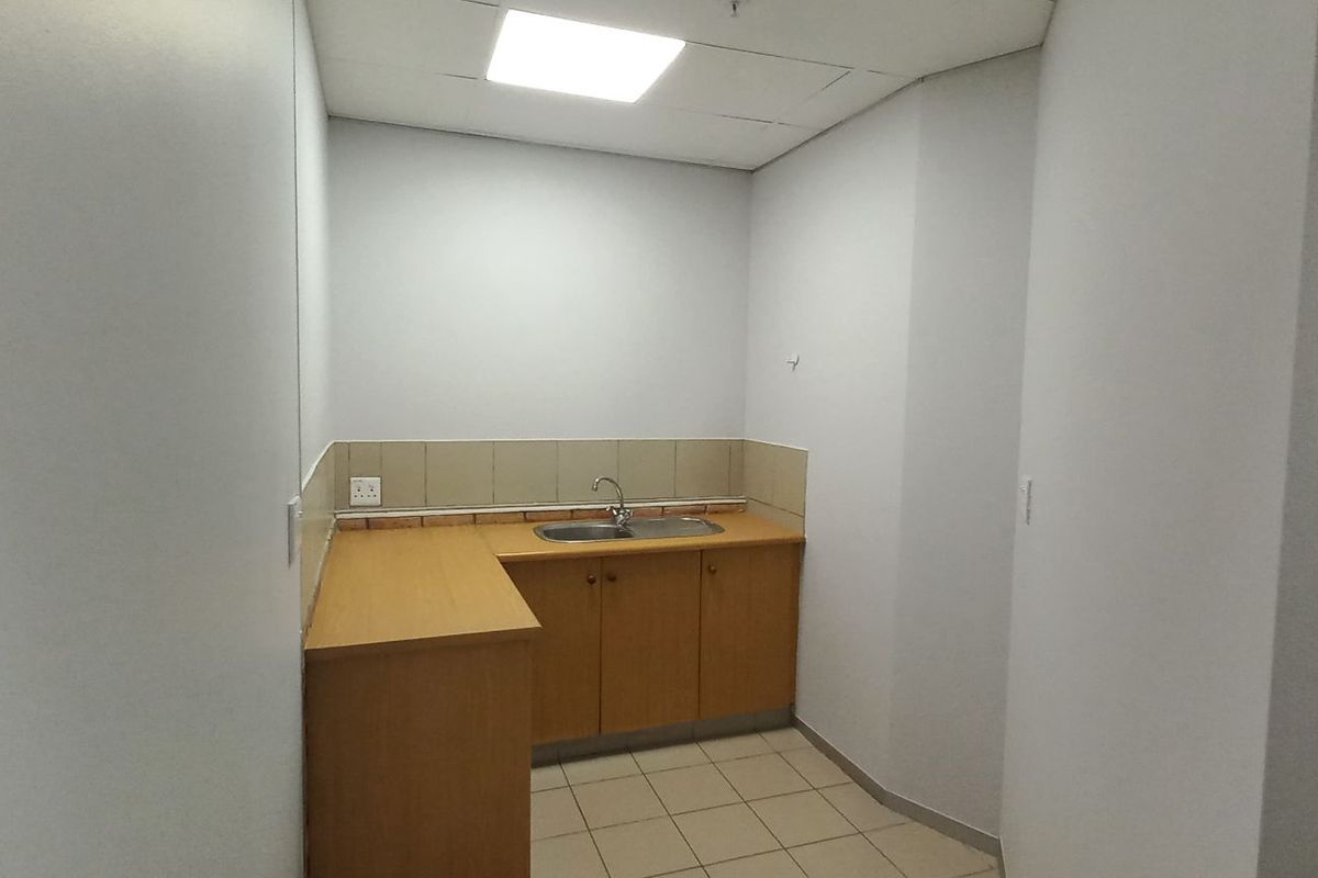 A functional kitchenette area featuring built-in wooden cabinetry, a stainless steel sink, tiled splashback, and neutral tiled flooring.