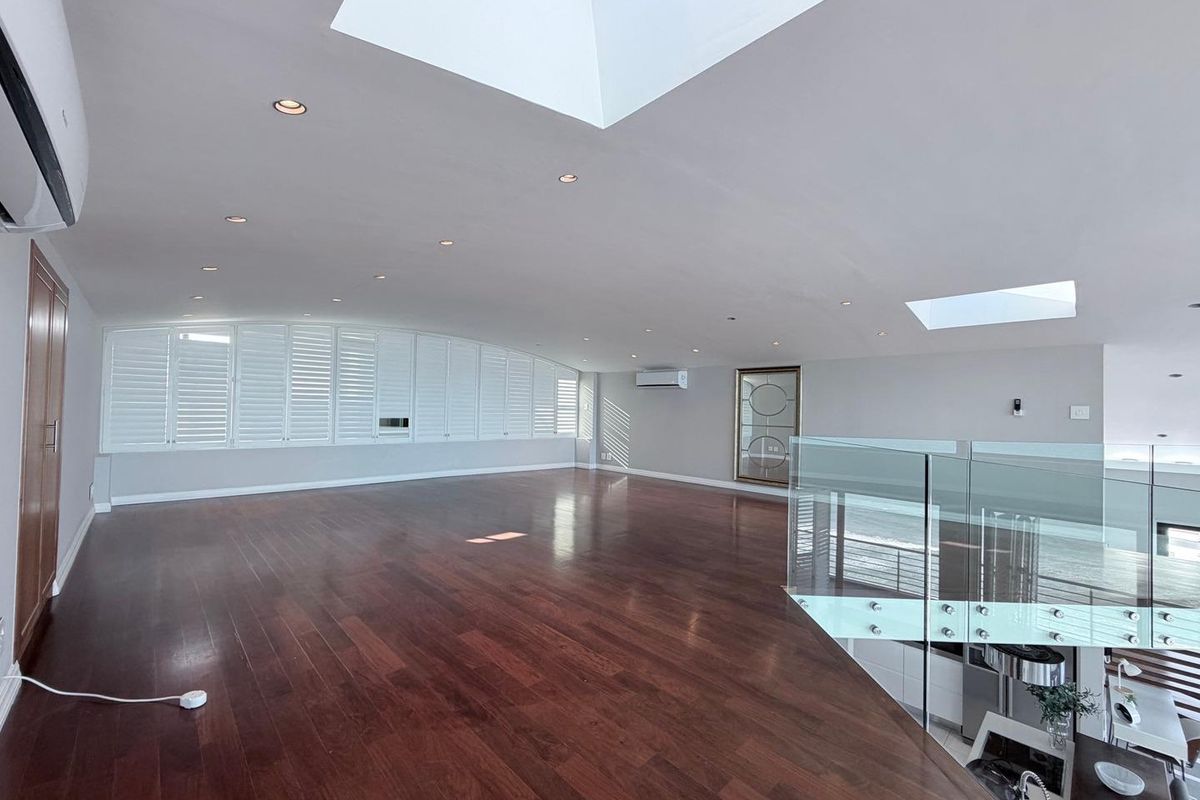 Spacious open-plan living area featuring polished hardwood floors, multiple skylights, recessed lighting, and a modern glass balustrade overlooking the lower level.