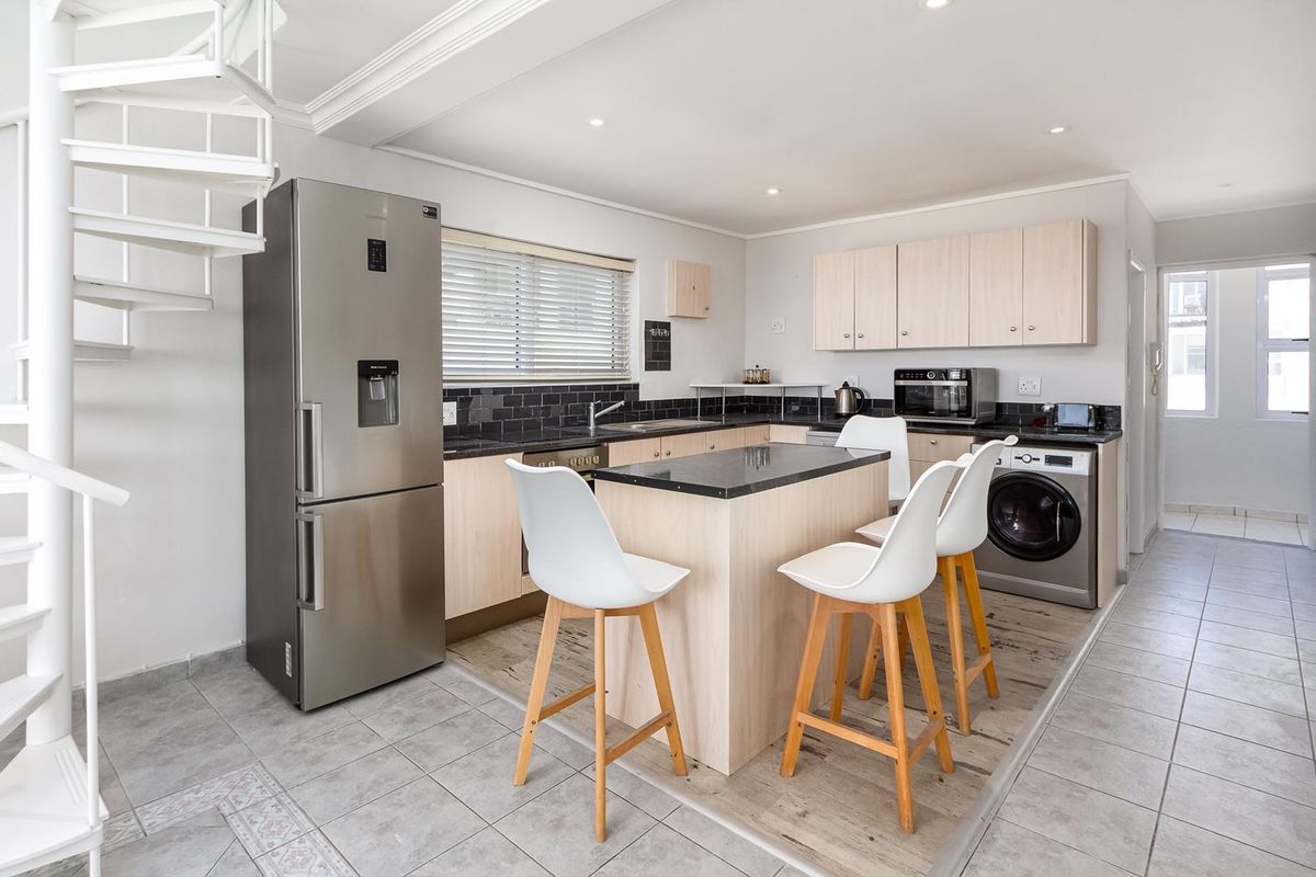 Modern kitchen featuring a central island, granite countertops, subway tile backsplash, and integrated appliances, complemented by a striking white spiral staircase.