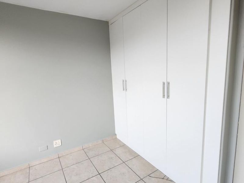 A clean, empty bedroom featuring neutral wall paint, tiled flooring, and ample built-in cupboard storage space.