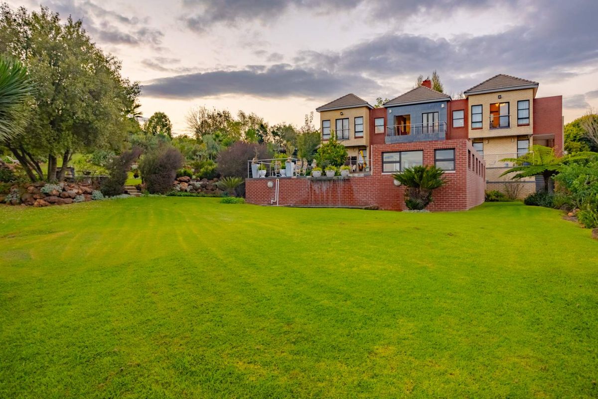 Rear view of a multi-story residential property featuring a large manicured lawn, brick exterior, and an elevated balcony overlooking the garden.