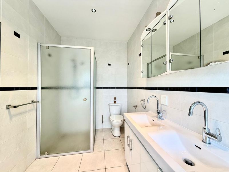 A clean, modern bathroom featuring a glass shower enclosure, a dual vanity with integrated sinks, and a mirrored medicine cabinet.