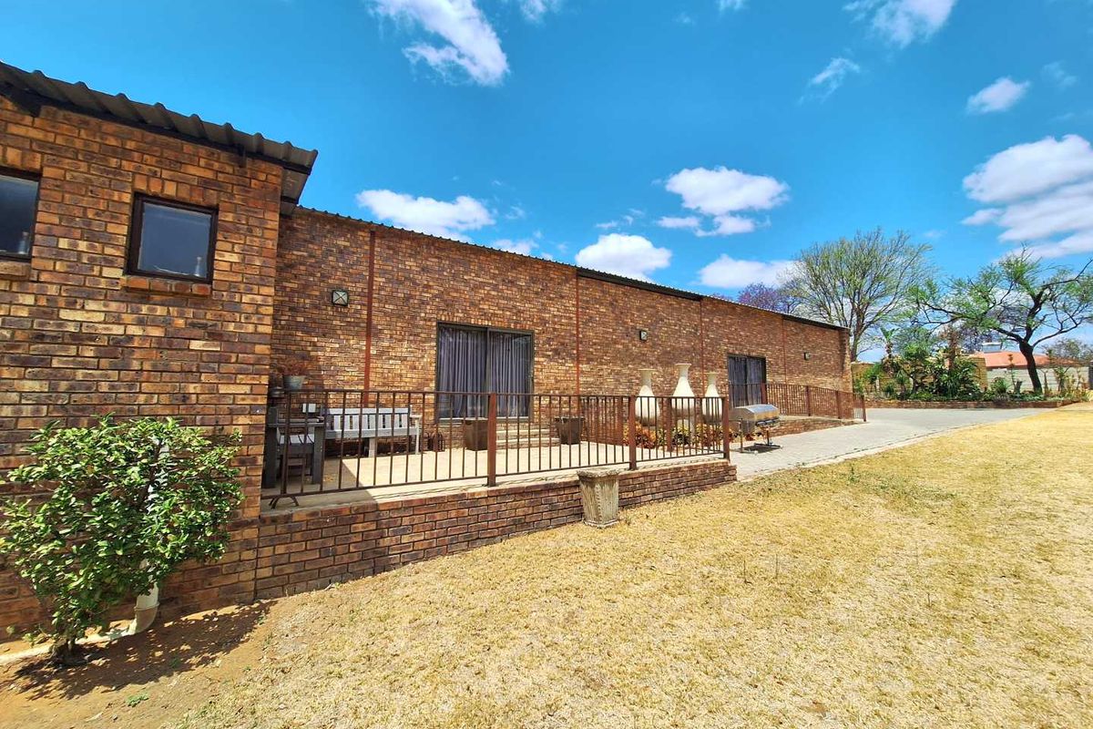 Rear view of a face-brick building featuring a covered patio area with metal railings and sliding door access to the interior.