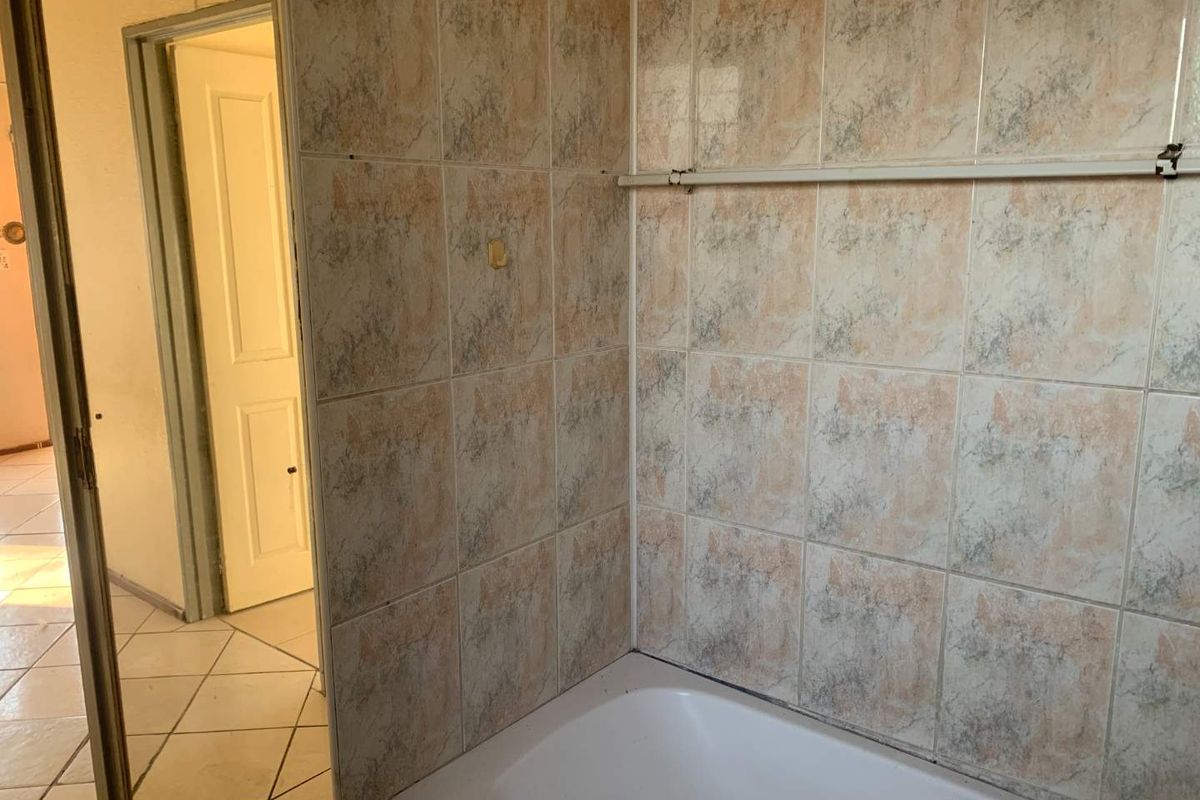 A dated bathroom featuring a standard bathtub with patterned wall tiling and a view into the adjacent hallway.