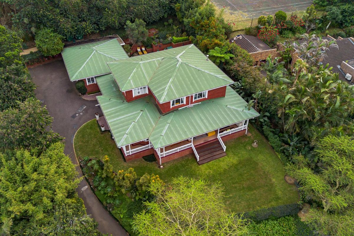 Aerial view of a detached house featuring a green corrugated metal roof, brick exterior, and surrounding landscaped gardens with a private driveway.
