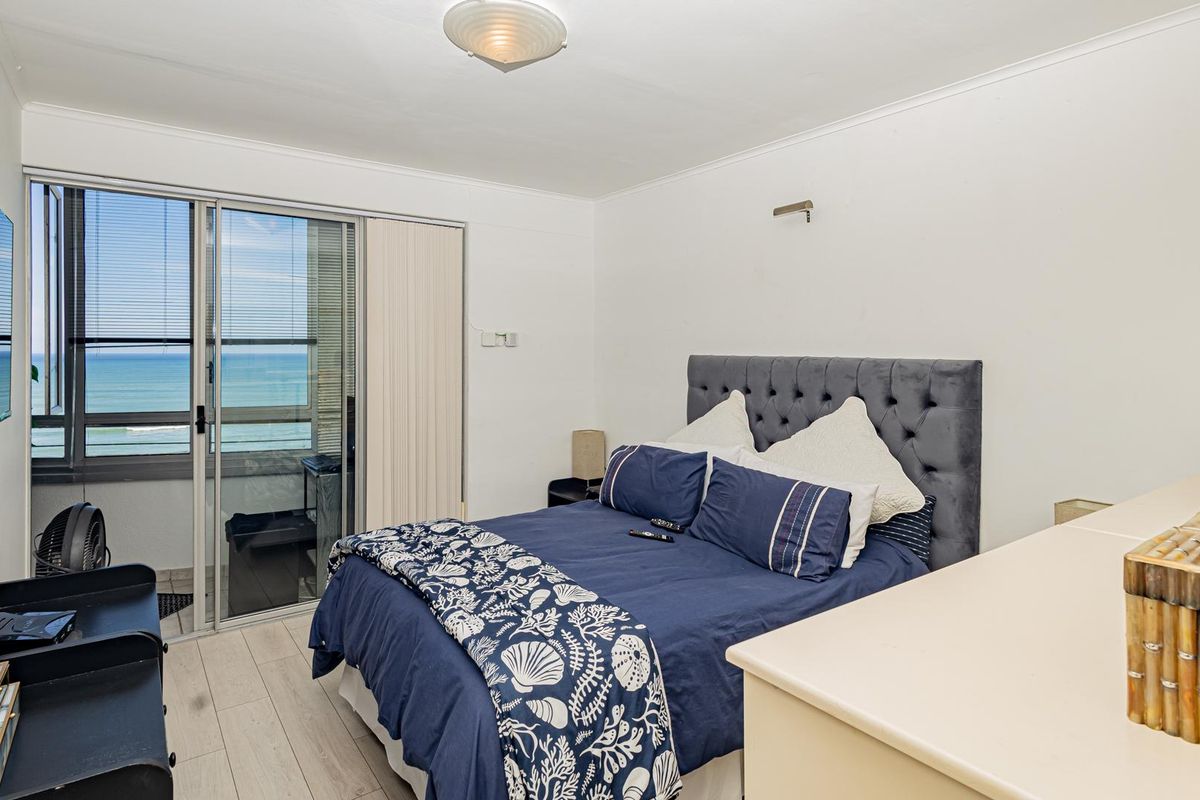 A bright bedroom featuring laminate flooring, a wall-mounted television, and sliding glass doors that open to a balcony with ocean views.