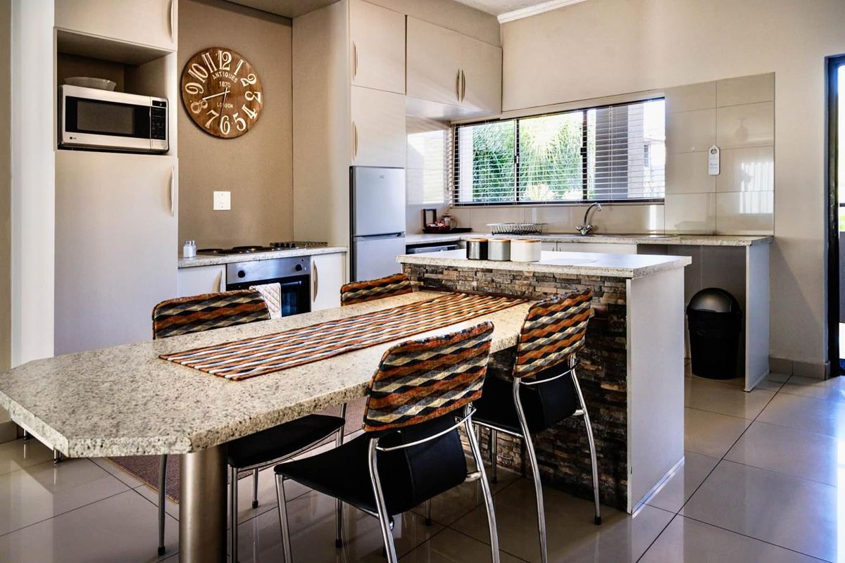 A functional kitchen featuring built-in cabinetry, granite countertops, a stone-clad breakfast bar, and integrated appliances, finished with neutral tiling throughout.