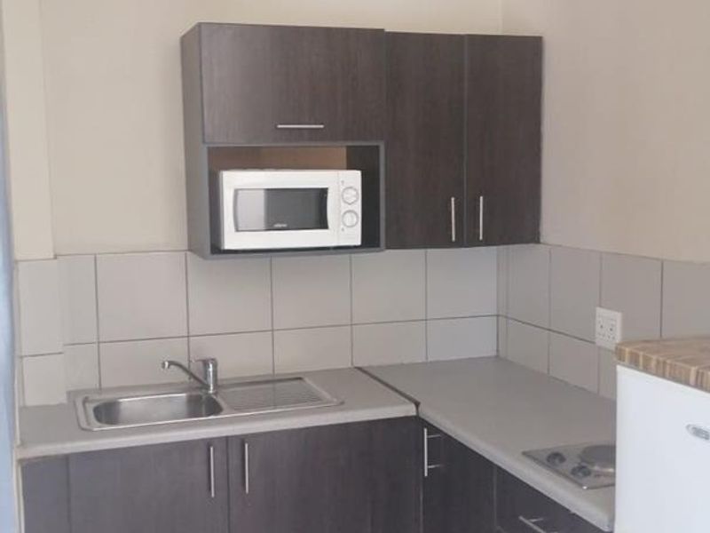Compact kitchen featuring dark wood-finish cabinetry, laminate countertops, a stainless steel sink, and tiled flooring with a functional layout.