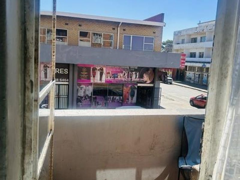 A small balcony area with concrete flooring and metal door frame, overlooking a street-level commercial building.