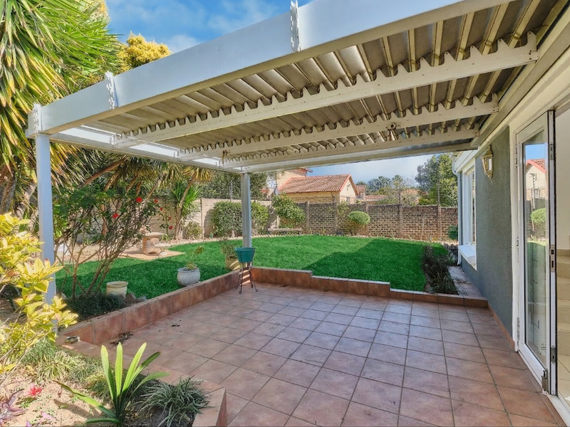 A covered patio area with tiled flooring, featuring a corrugated roof structure and direct access to a private rear garden.
