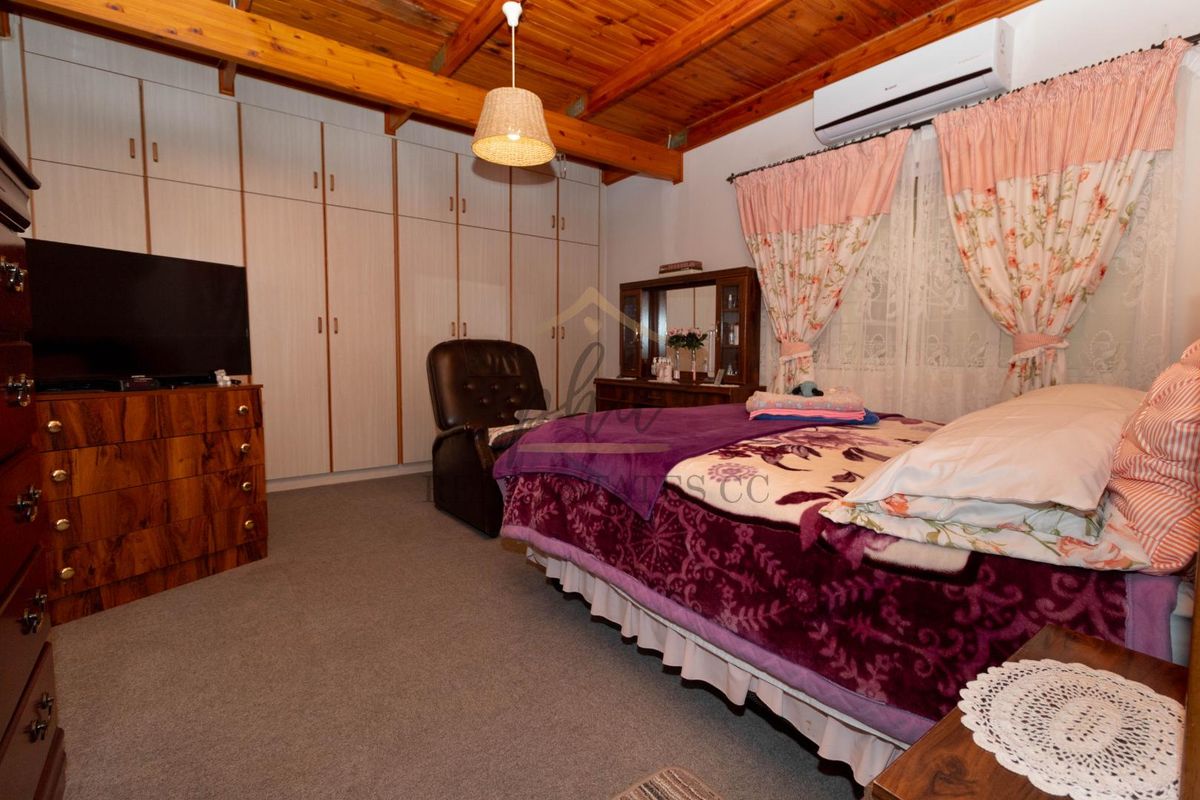 A bedroom featuring exposed timber ceiling beams, wall-to-wall built-in cabinetry, and a wall-mounted air conditioning unit.