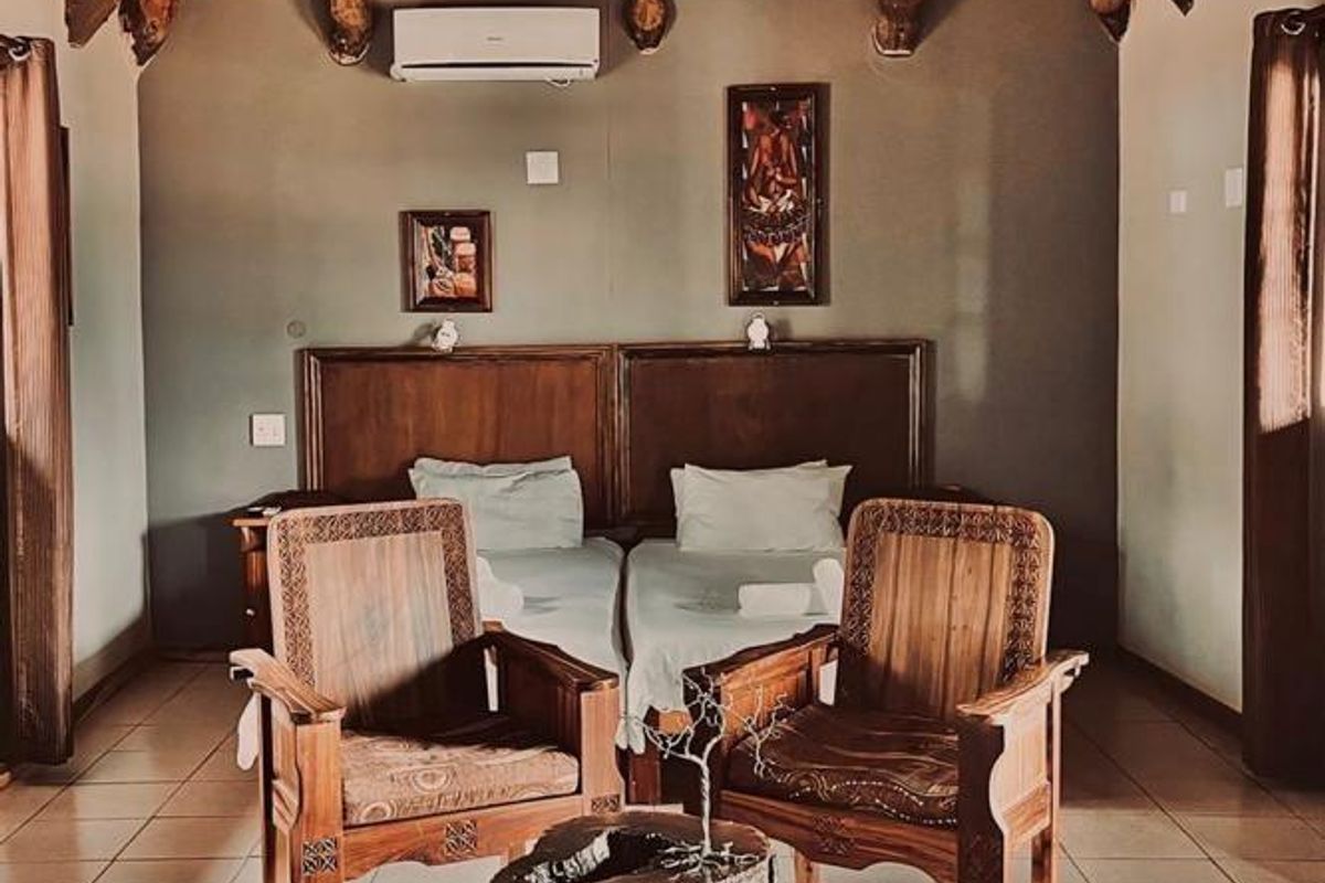 A spacious bedroom featuring a traditional thatched roof, exposed timber beams, tiled flooring, and a wall-mounted air conditioning unit.