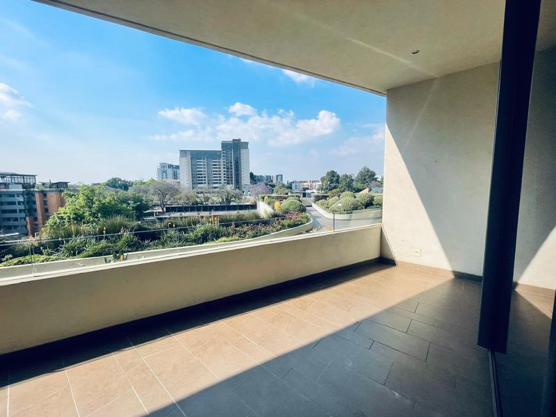 A spacious, modern balcony featuring tiled flooring and a sleek glass balustrade, offering expansive views of the surrounding urban landscape.