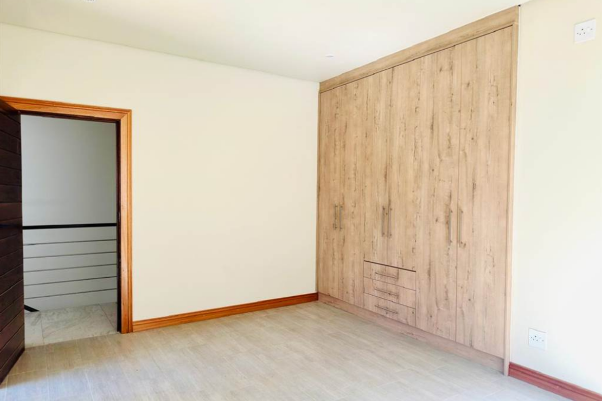 A bright, empty bedroom featuring modern wood-grain built-in cupboards and tiled flooring, providing a clean and neutral space ready for personalization.