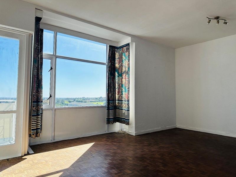 A bright, empty living room featuring classic parquet flooring, large windows with natural light, and access to an outdoor balcony area.