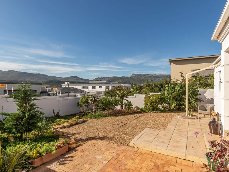 A well-maintained rear garden featuring a paved patio area, gravel landscaping, and a boundary wall with electric fencing, offering scenic mountain views.