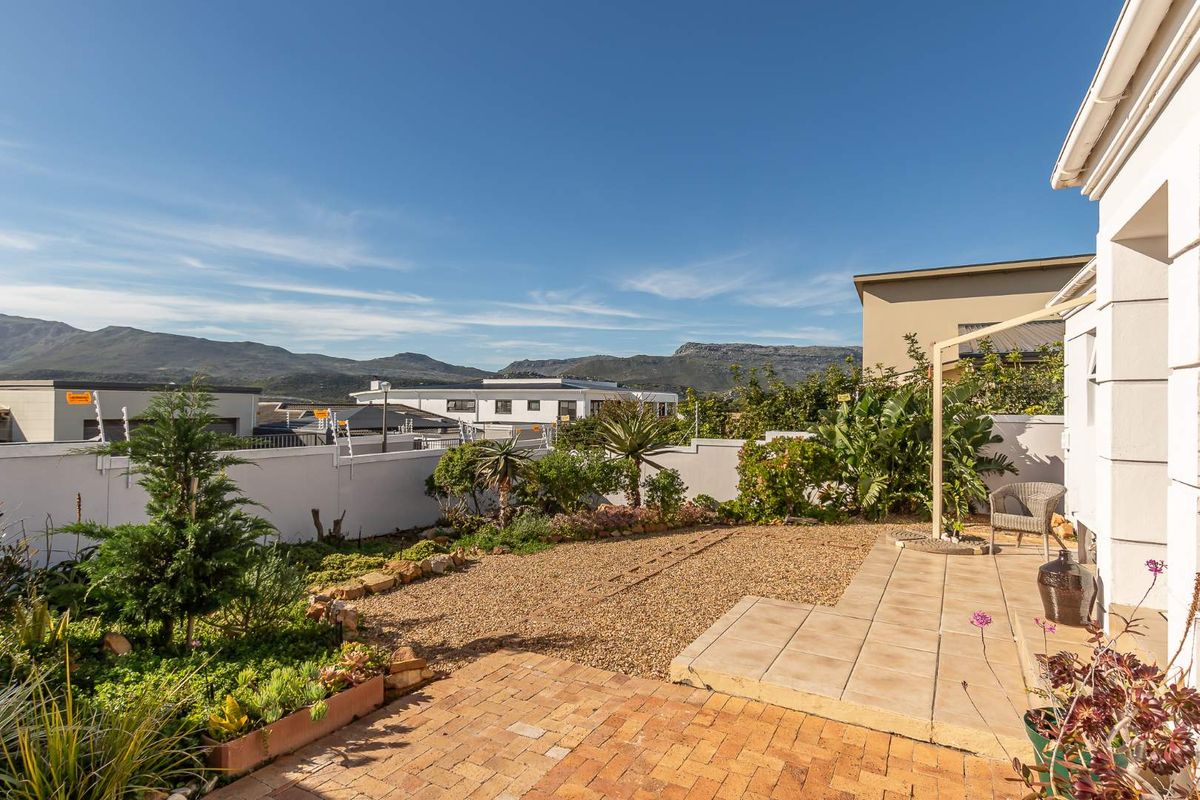 A well-maintained rear garden featuring a paved patio area, gravel landscaping, and a boundary wall with electric fencing, offering scenic mountain views.