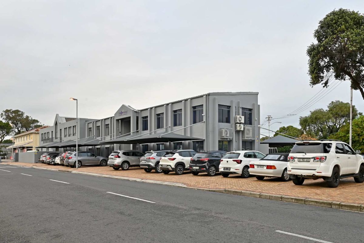 A multi-story commercial building featuring a paved parking area with shade cloth carports and external air conditioning units.