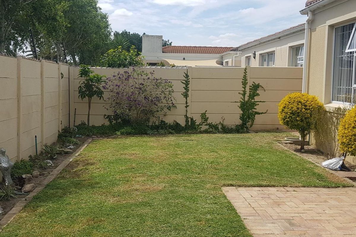 A private rear garden featuring a paved patio area, a small lawn, and perimeter boundary walls.