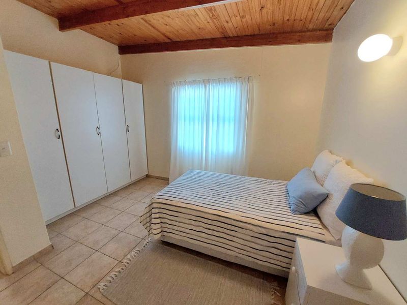 A bedroom featuring tiled flooring, built-in cupboards, and an exposed timber ceiling, providing a functional and neutral living space.