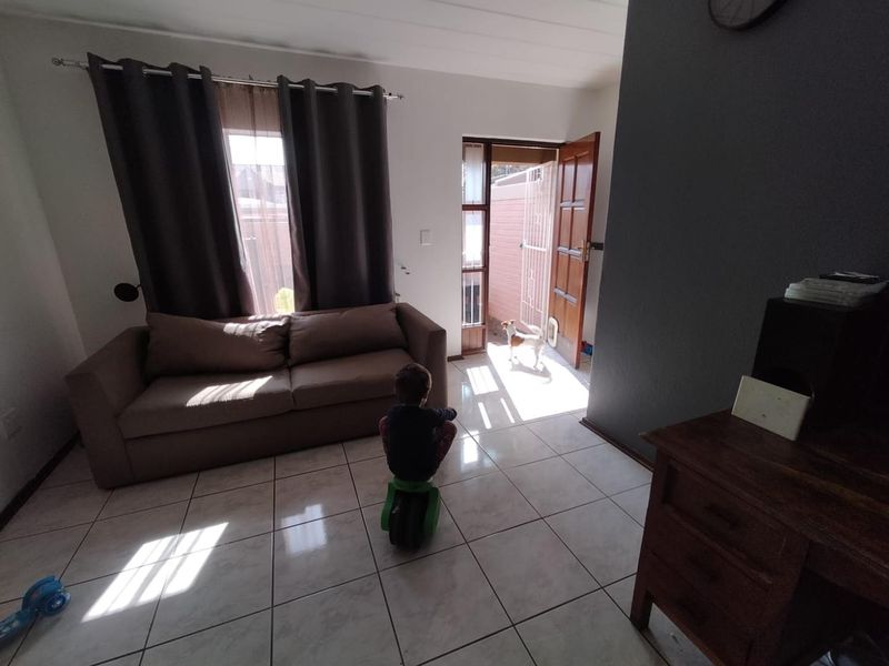 A living room area featuring tiled flooring and direct access to an outdoor space through a timber door with a security gate.