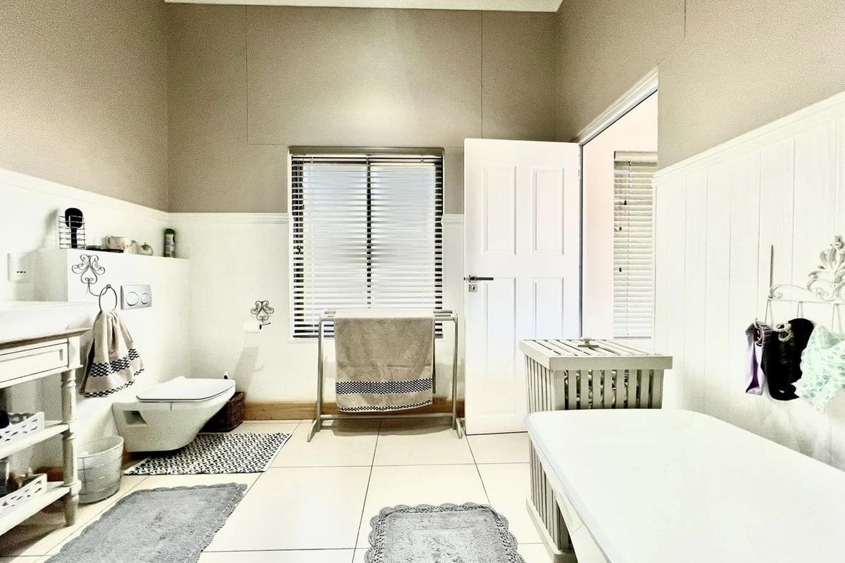 A bright, well-maintained bathroom featuring a wall-mounted toilet, a freestanding bathtub, and classic wainscoting paneling with neutral wall tones.