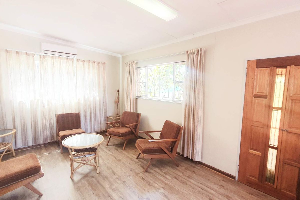 A bright living room featuring wood-look flooring, a wall-mounted air conditioning unit, and a solid timber entrance door with glass panel inserts.