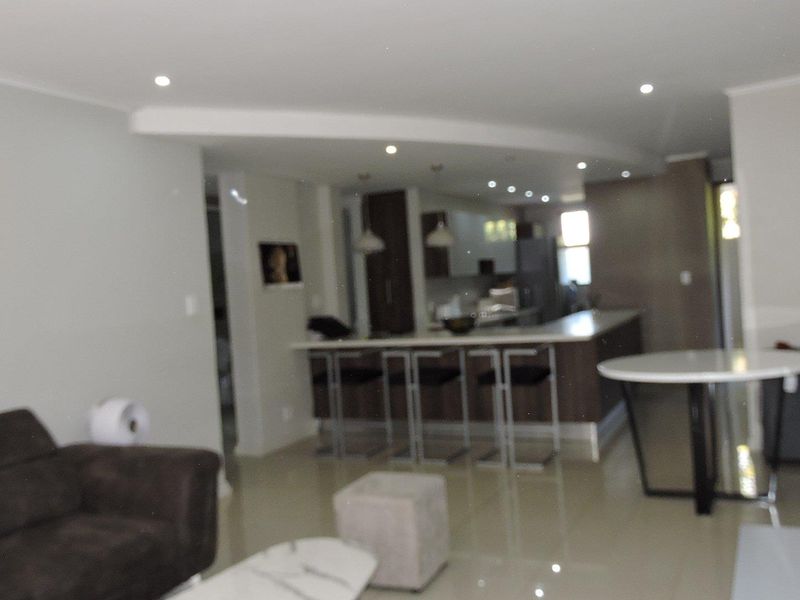 Open plan living and kitchen area featuring a breakfast bar, recessed lighting, and tiled flooring in a modern apartment setting.
