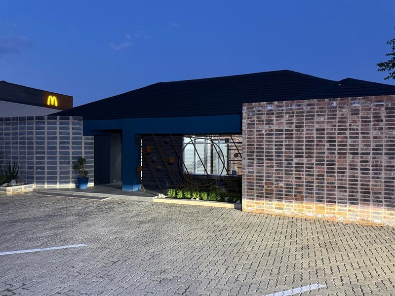 Front exterior view of a commercial property featuring a modern brick facade, dark tiled roof, and a paved driveway area.