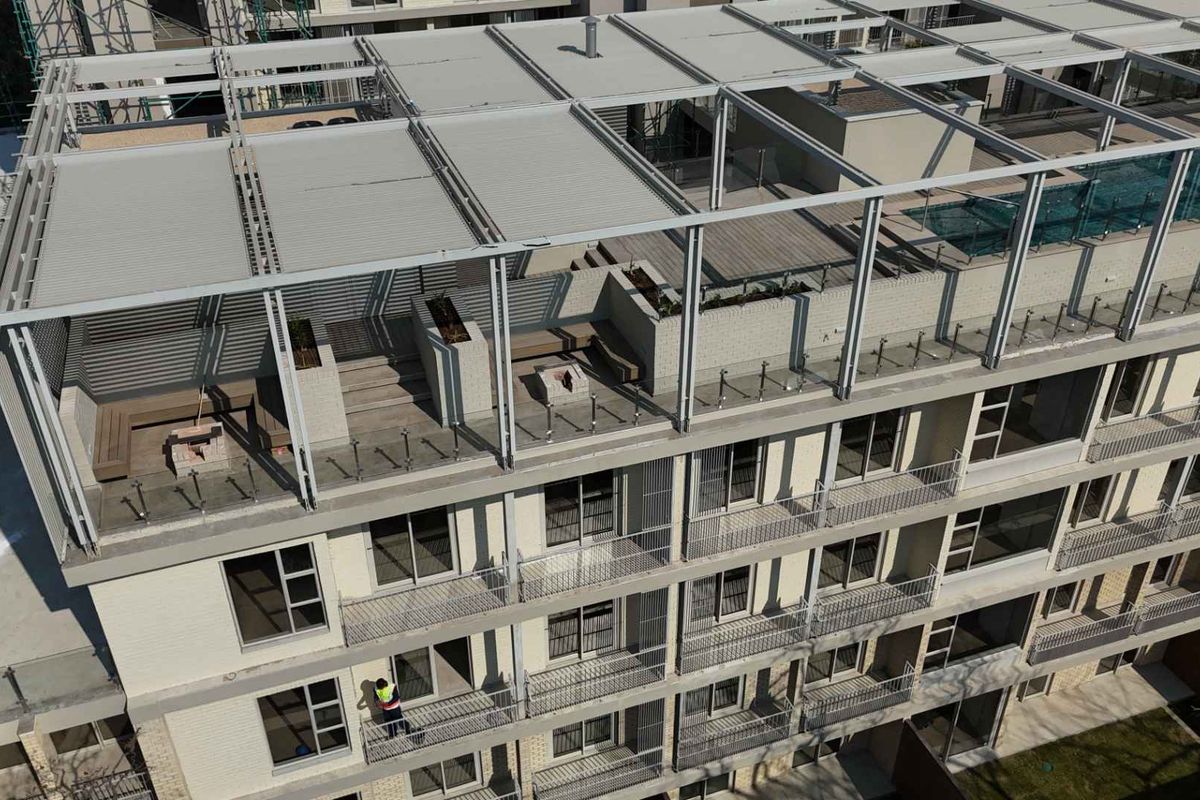 Aerial view of a modern apartment building featuring a rooftop terrace with a pool, fire pit, and private balconies on each level.