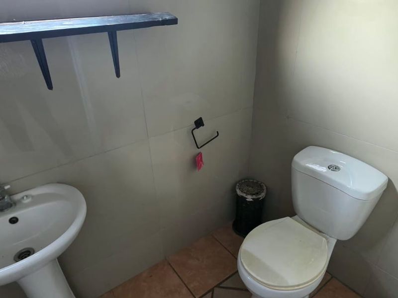A compact bathroom featuring a pedestal washbasin, standard toilet, and neutral wall tiling. The space is functional but would benefit from cosmetic updates.