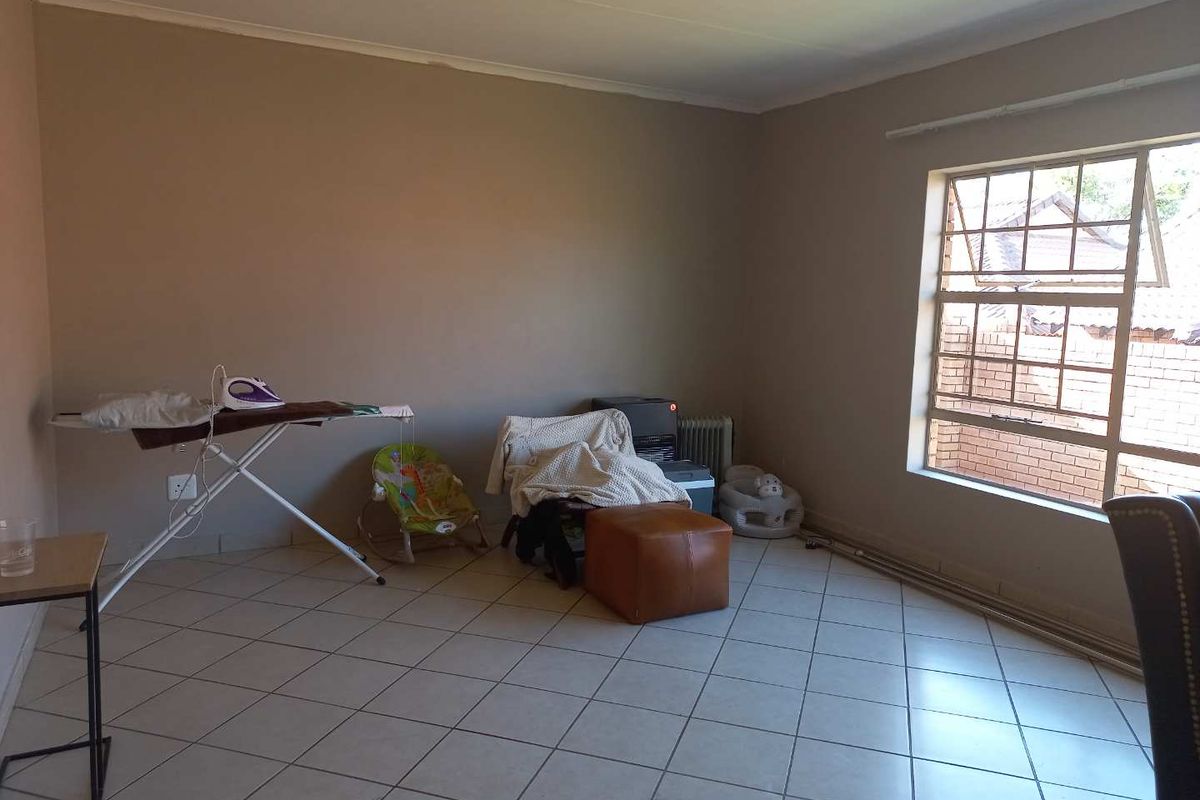 A spacious living room featuring neutral wall tones, tiled flooring, and a large window providing natural light.