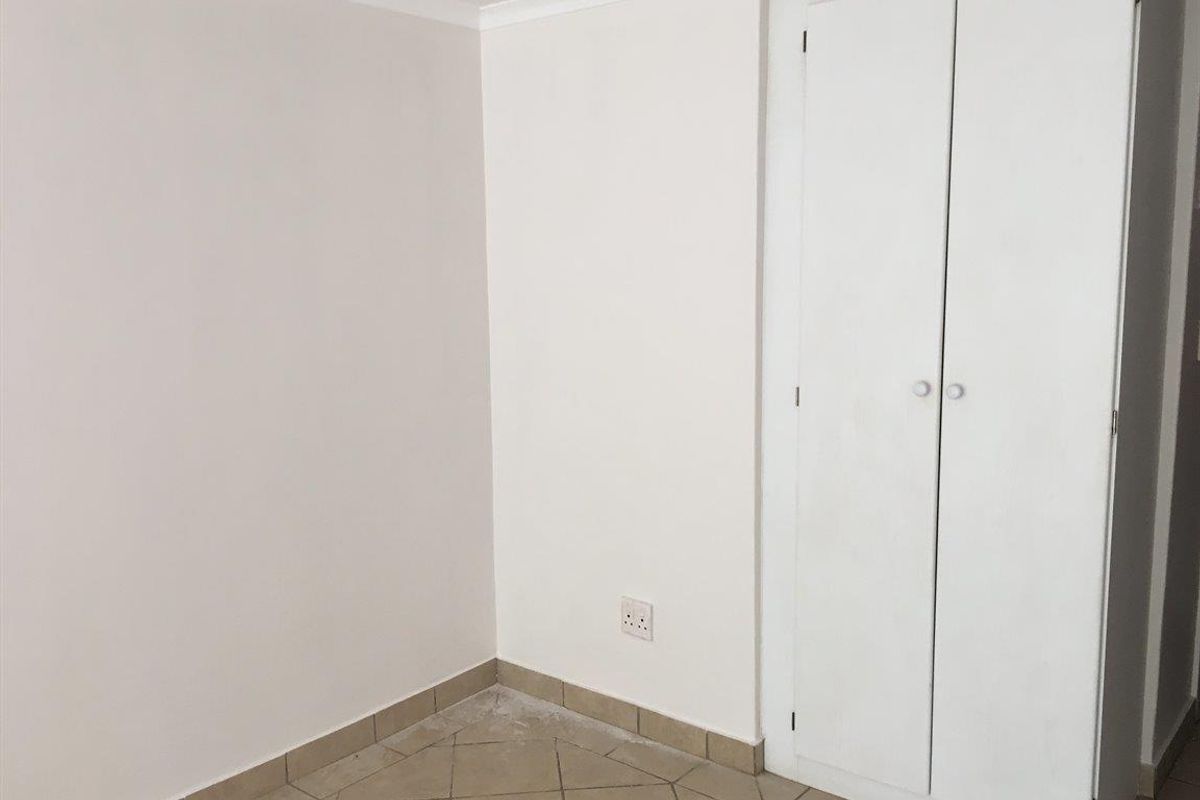 A simple, empty bedroom featuring tiled flooring and a built-in wardrobe with white cabinetry.