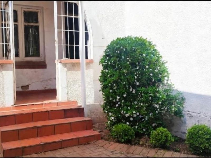 Front entrance area featuring tiled steps, security gate, and window bars, showing signs of weathered exterior plaster and paintwork.