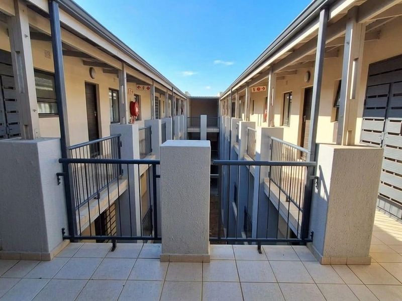 An exterior view of an apartment complex corridor featuring tiled walkways, metal balustrades, and access to multiple residential units.