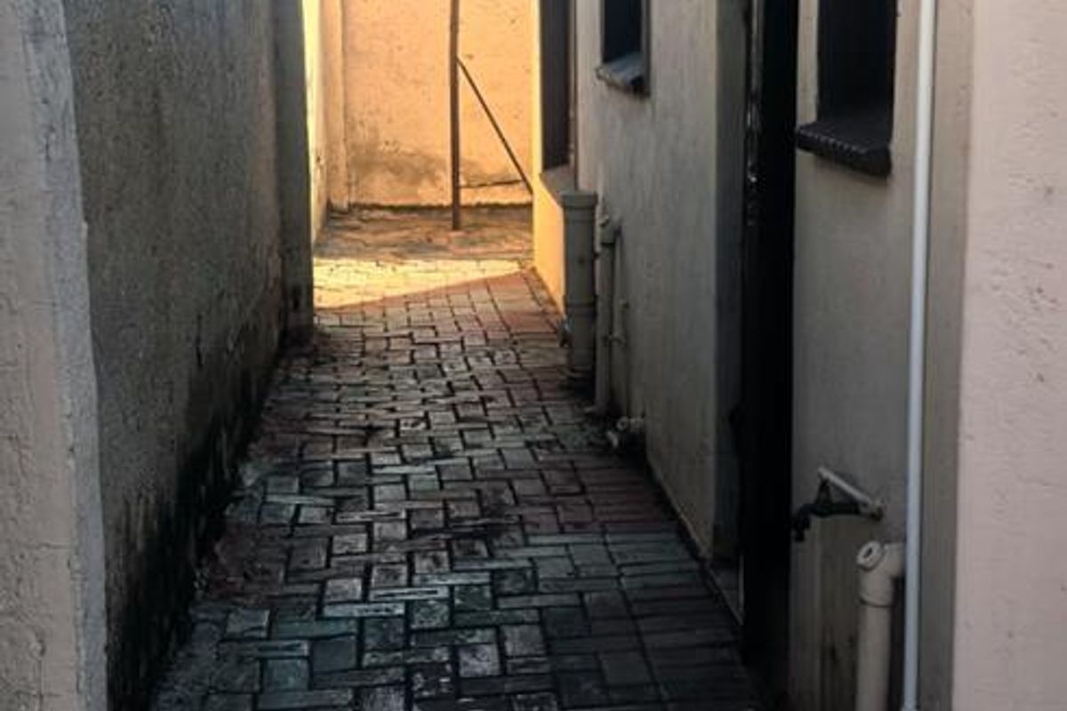 A narrow side exterior passage featuring paved flooring, a wall-mounted awning, and external plumbing fixtures.