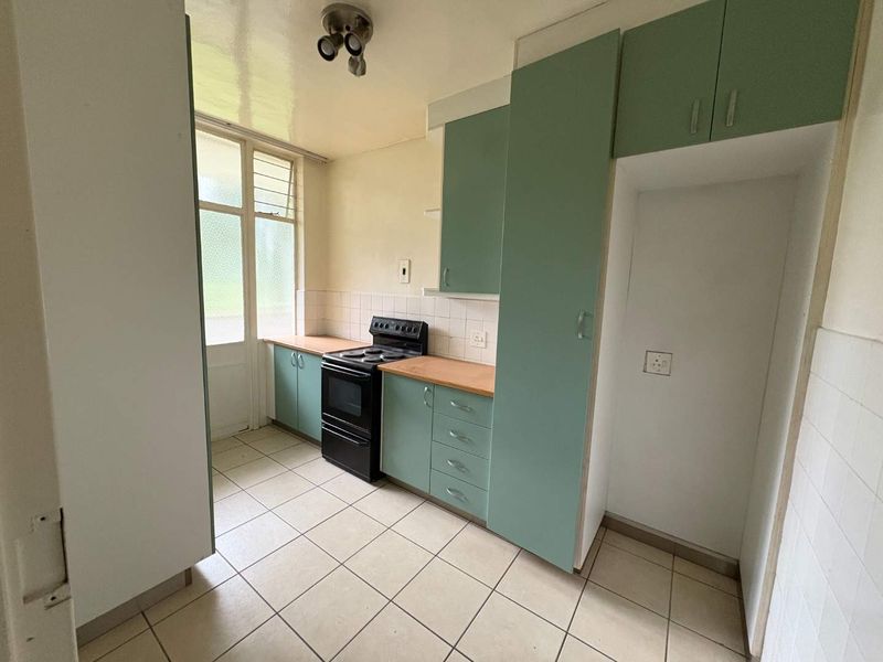 A functional kitchen featuring light green cabinetry, tiled flooring, a tiled backsplash, and a freestanding stove, offering a blank canvas for modern updates.