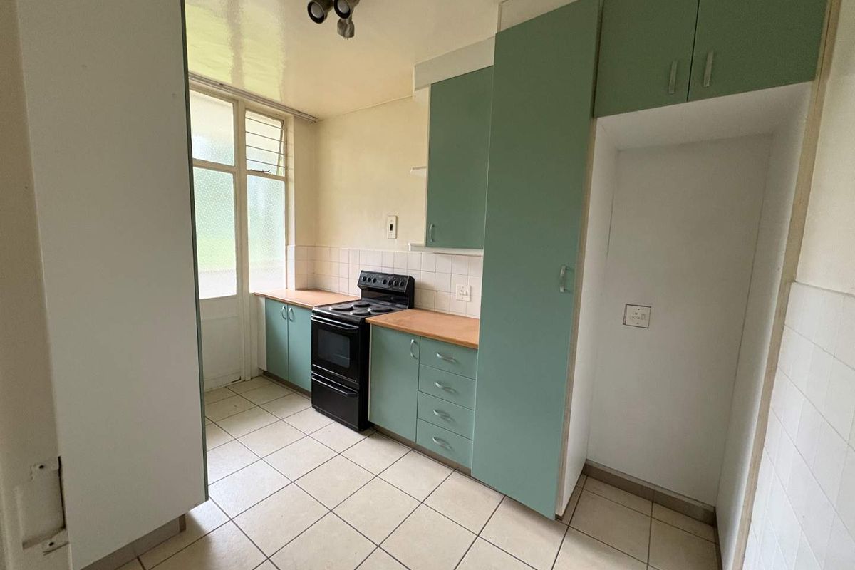 A functional kitchen featuring light green cabinetry, tiled flooring, a tiled backsplash, and a freestanding stove, offering a blank canvas for modern updates.