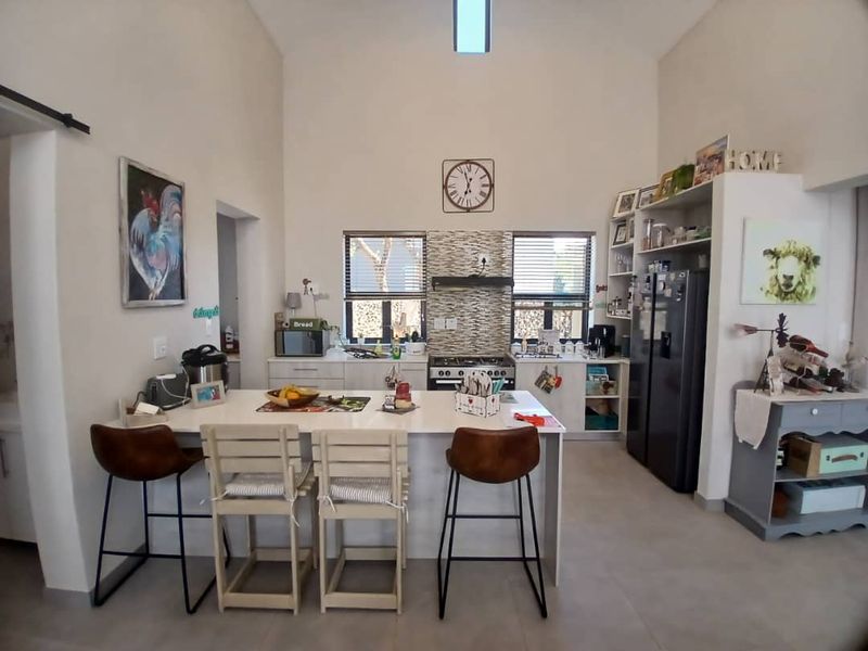 Spacious kitchen featuring a central island, built-in oven and hob, tiled splashback, and a high vaulted ceiling with a skylight for natural light.