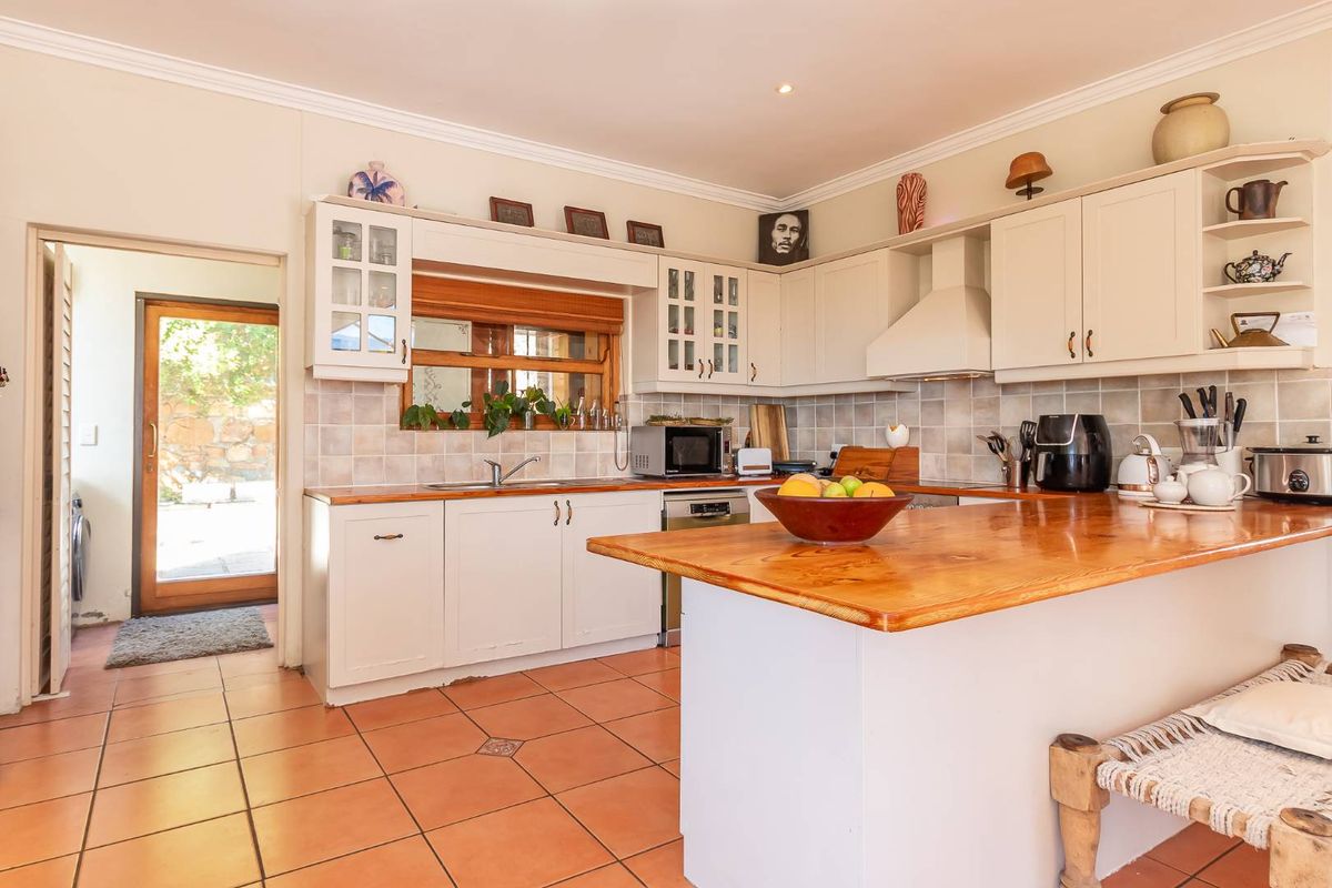A functional kitchen featuring timber countertops, tiled flooring, built-in cabinetry, and an integrated extractor fan, with direct access to an outdoor area.